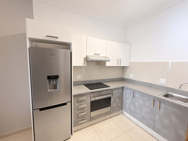 Modern kitchen featuring granite countertops, built-in oven, electric hob, extractor fan, and ample cabinetry, finished with neutral tiled flooring.