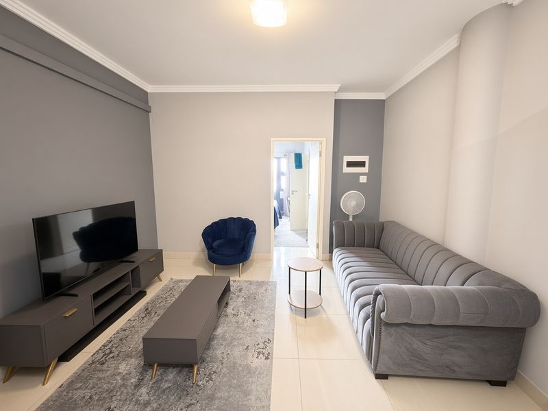 A well-maintained living room featuring neutral grey walls, tiled flooring, and crown molding, providing a clean and modern aesthetic.
