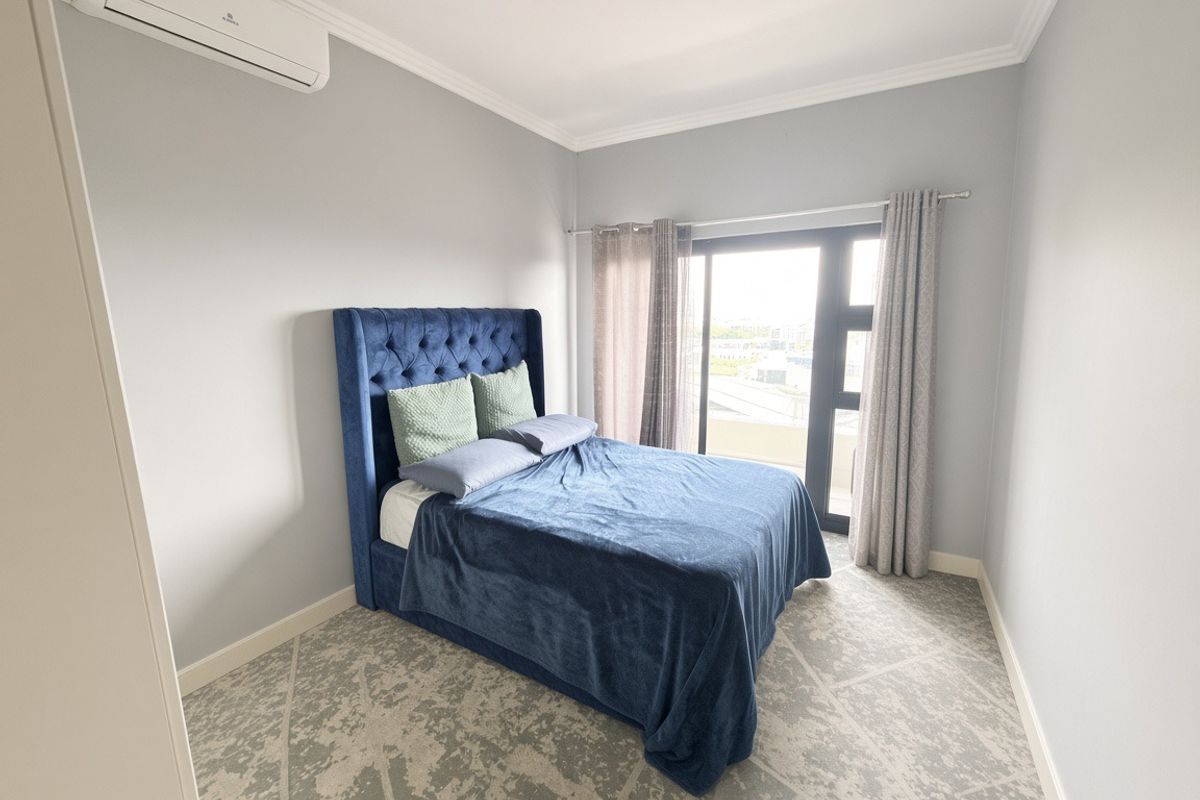 A well-maintained bedroom featuring a split-system air conditioner, crown molding, and a sliding glass door providing natural light and access to the exterior.