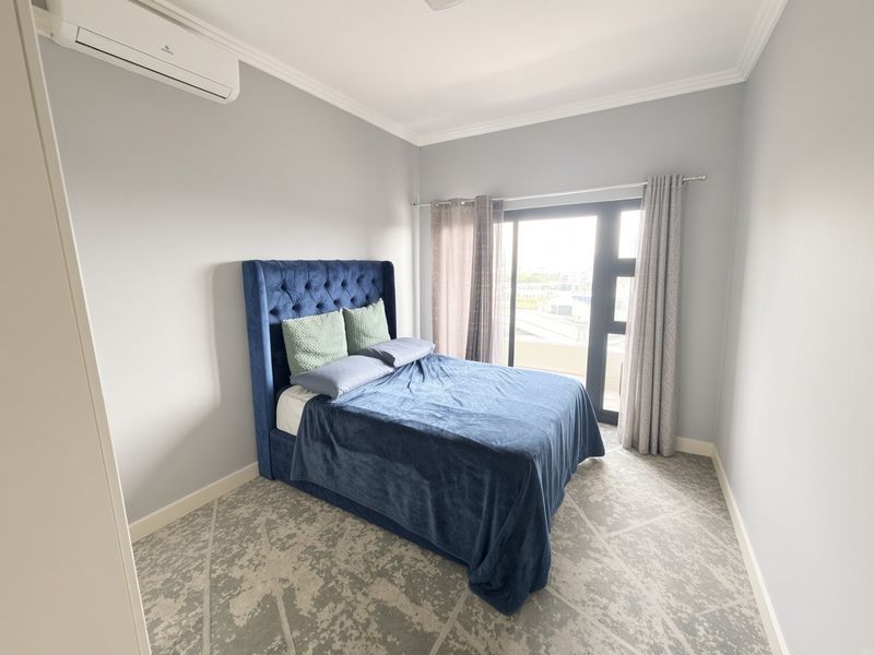 A well-maintained bedroom featuring a split-system air conditioner, crown molding, and a sliding glass door providing natural light and access to the exterior.