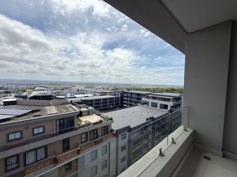 A modern apartment balcony featuring a glass balustrade and tiled flooring, offering an expansive elevated view of the surrounding urban landscape.