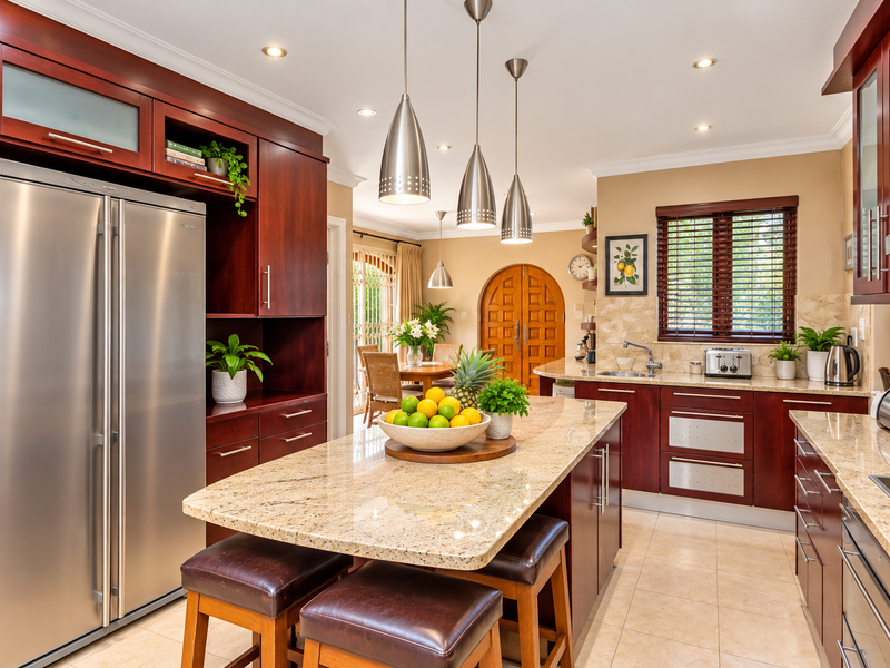 A well-appointed kitchen featuring rich cherry wood cabinetry, granite countertops, a central island with breakfast seating, and modern stainless steel appliances.