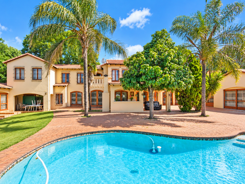Spacious rear exterior featuring a large swimming pool, extensive brick-paved patio area, mature palm trees, and a well-maintained Mediterranean-style home facade.