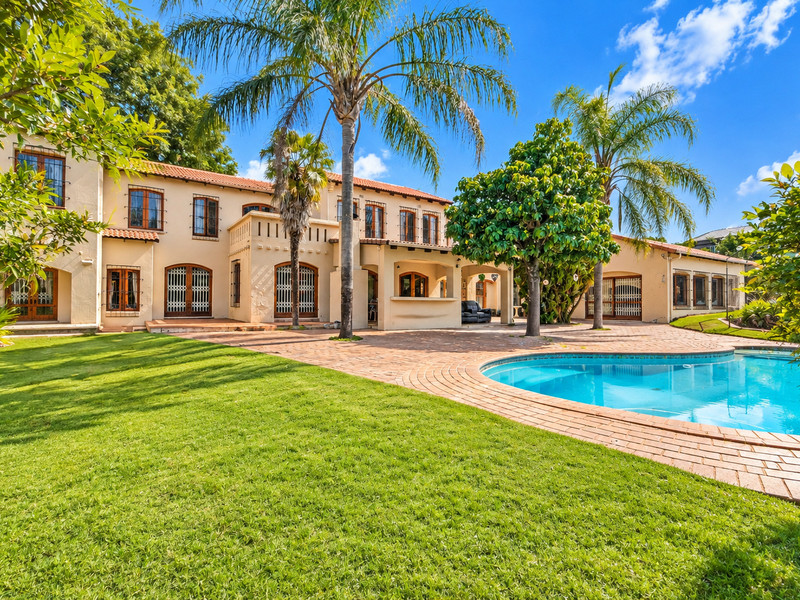 Spacious rear exterior featuring a large swimming pool, brick-paved patio, covered veranda, and well-maintained garden with mature trees.