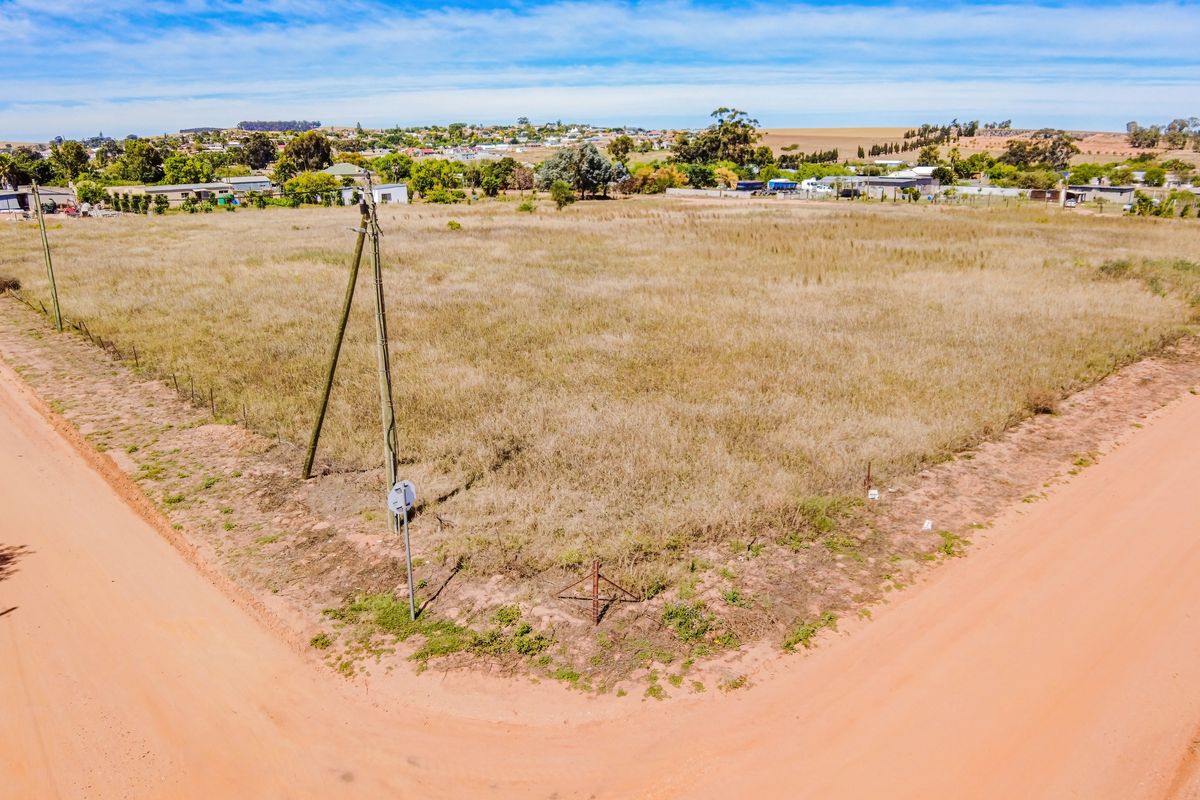 An elevated aerial view of a vacant residential plot situated on a corner lot with dirt road access and existing utility infrastructure.