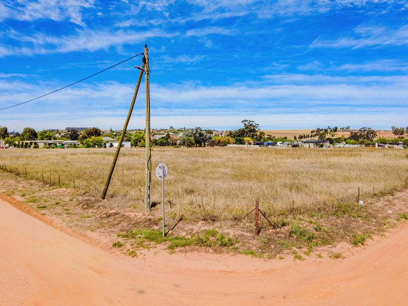 A vacant residential plot of land situated on a corner lot with dirt road access and existing utility infrastructure.
