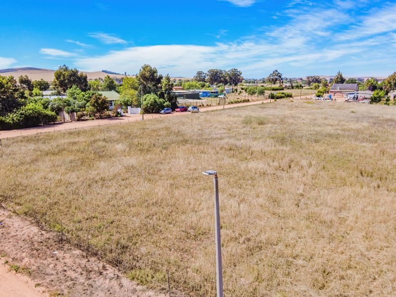 An aerial view of a vacant residential plot featuring dry grass, perimeter wire fencing, and a street light.