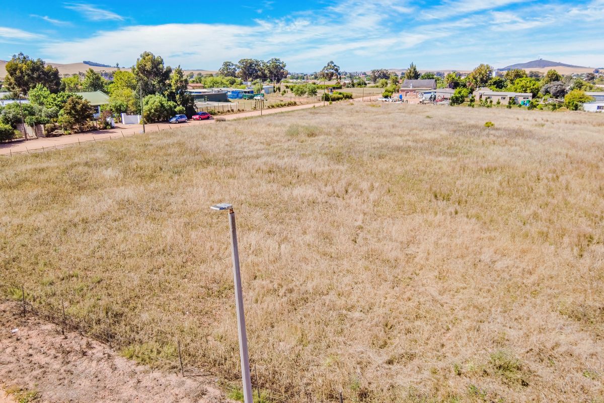 An elevated aerial view of a vacant residential plot featuring dry grass, perimeter wire fencing, and a street light pole.