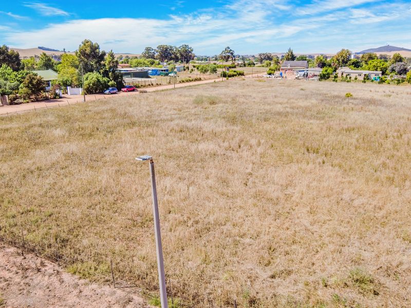 An elevated aerial view of a vacant residential plot featuring dry grass, perimeter wire fencing, and a street light pole.