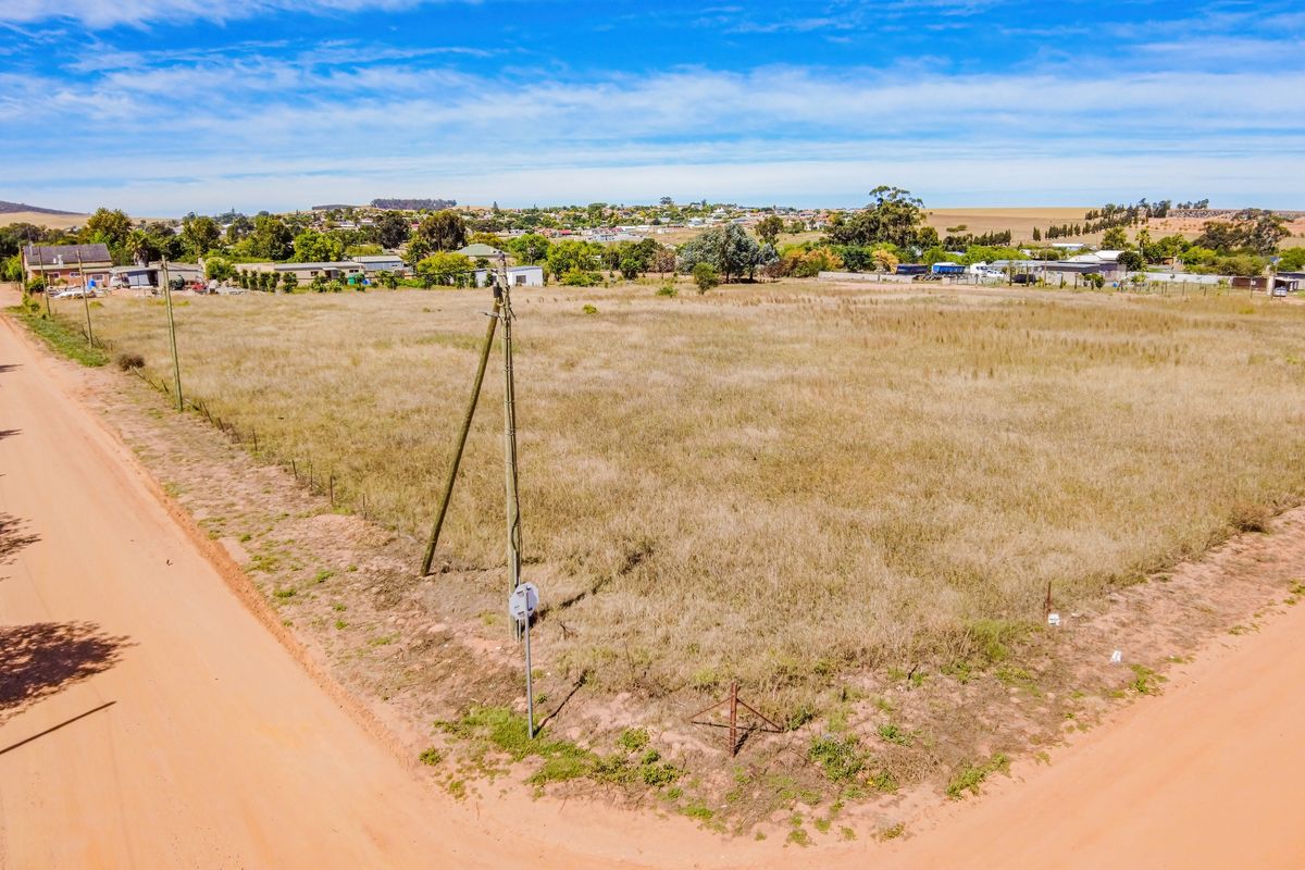 An aerial view of a vacant residential plot featuring dry grass, perimeter wire fencing, and utility poles, situated in a quiet neighborhood setting.