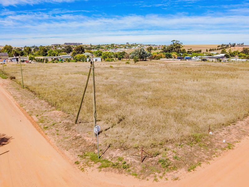 An aerial view of a vacant residential plot featuring dry grass, perimeter wire fencing, and utility poles, situated in a quiet neighborhood setting.
