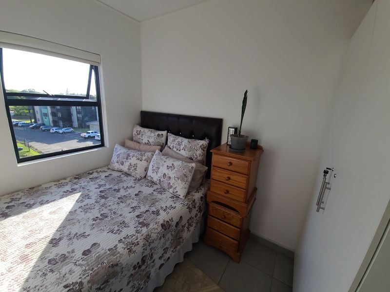 A compact bedroom featuring tiled flooring, a built-in wardrobe, and a window providing natural light and views of the surrounding area.