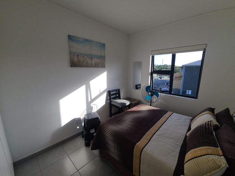 A functional bedroom featuring tiled flooring, an aluminium-framed window, and built-in storage, offering a bright and practical living space.