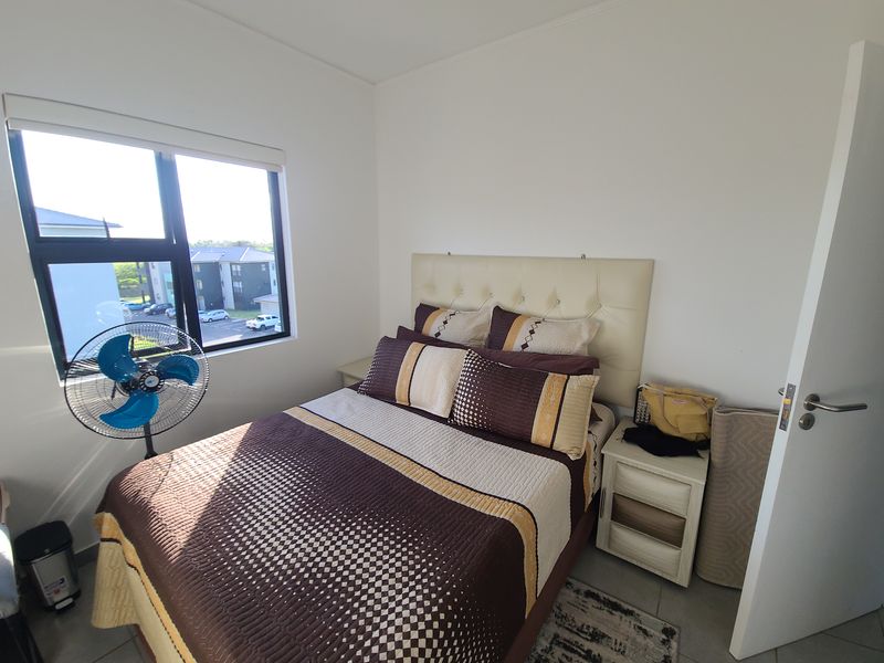 A functional bedroom featuring tiled flooring and a large window providing natural light and views of the surrounding apartment complex.