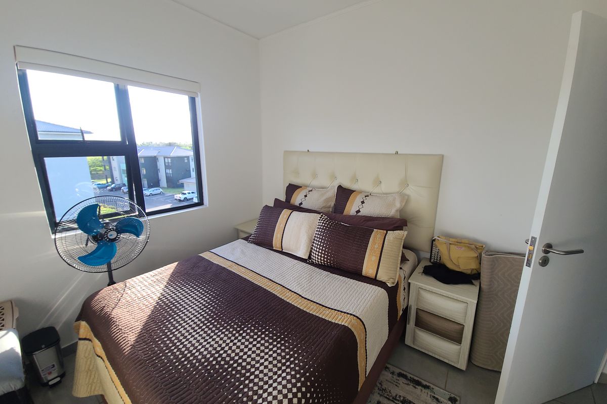 A functional bedroom featuring tiled flooring and a large window providing natural light and views of the surrounding apartment complex.
