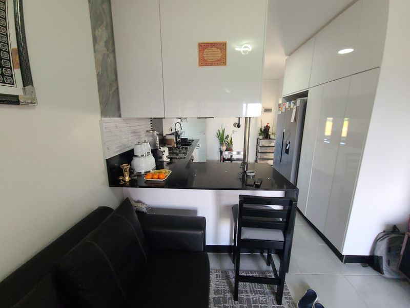 A modern open-plan kitchen featuring sleek white cabinetry, a black granite breakfast bar, and a tiled backsplash, seamlessly integrated into the living space.
