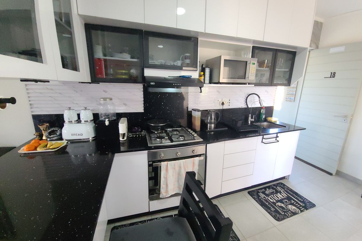 A modern kitchen featuring white cabinetry, black granite countertops, a gas hob, built-in oven, and a tiled backsplash.