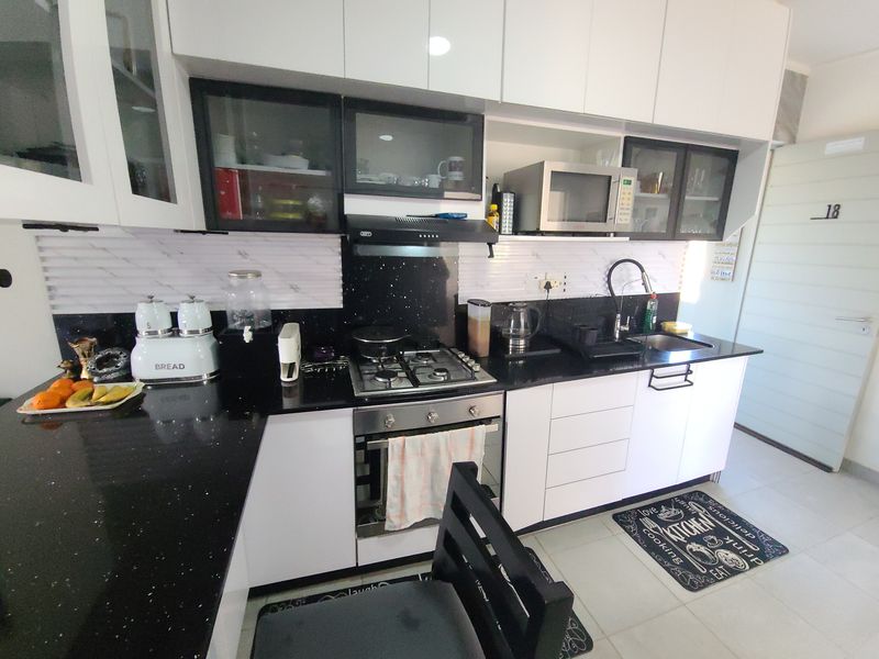 A modern kitchen featuring white cabinetry, black granite countertops, a gas hob, built-in oven, and a tiled backsplash.