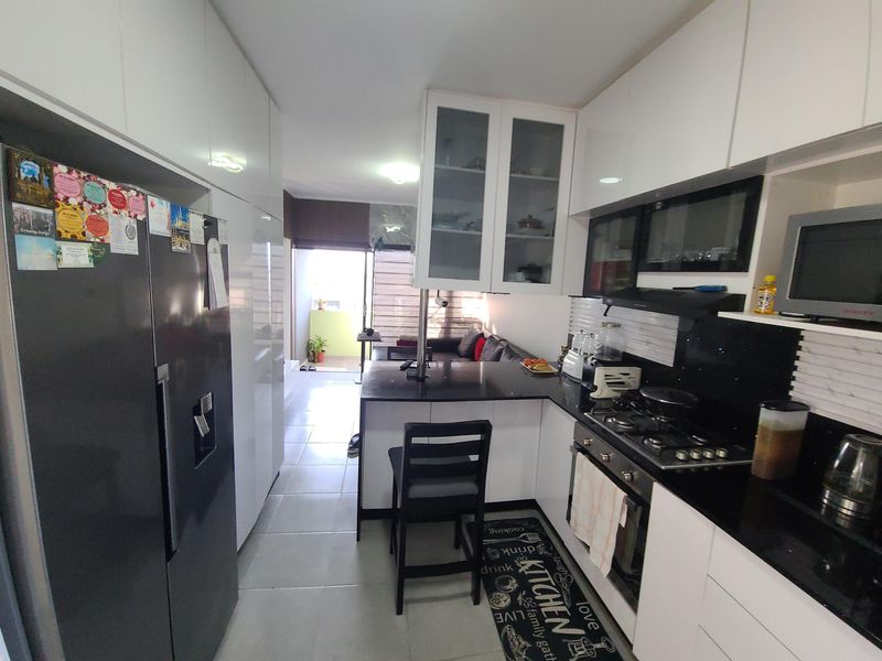 Modern open-plan kitchen featuring sleek white cabinetry, black granite countertops, integrated gas hob, and oven, flowing seamlessly into the adjacent living area.