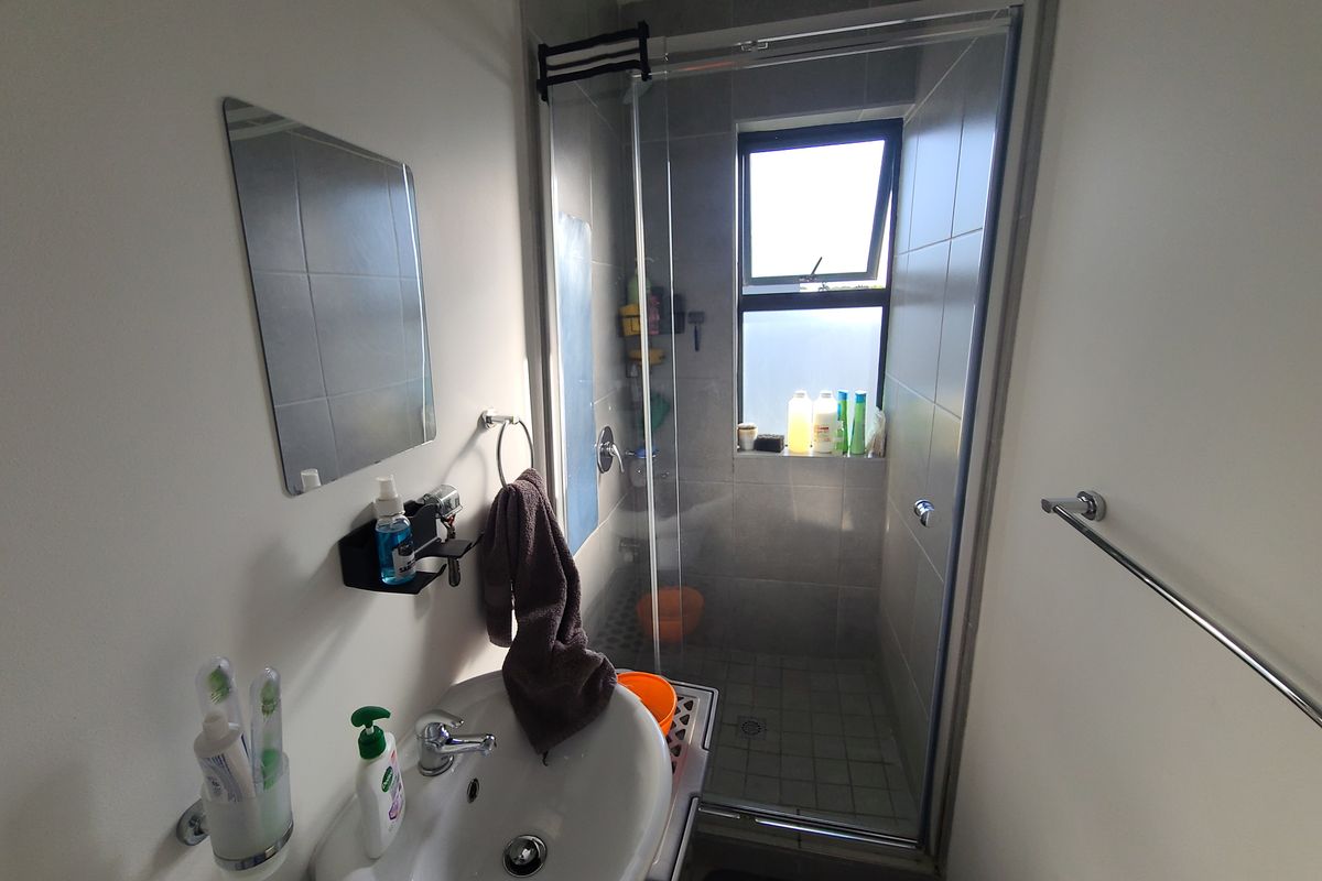 A compact bathroom featuring a pedestal basin, a glass-enclosed shower with tiled finishes, and a top-hung window for natural light and ventilation.