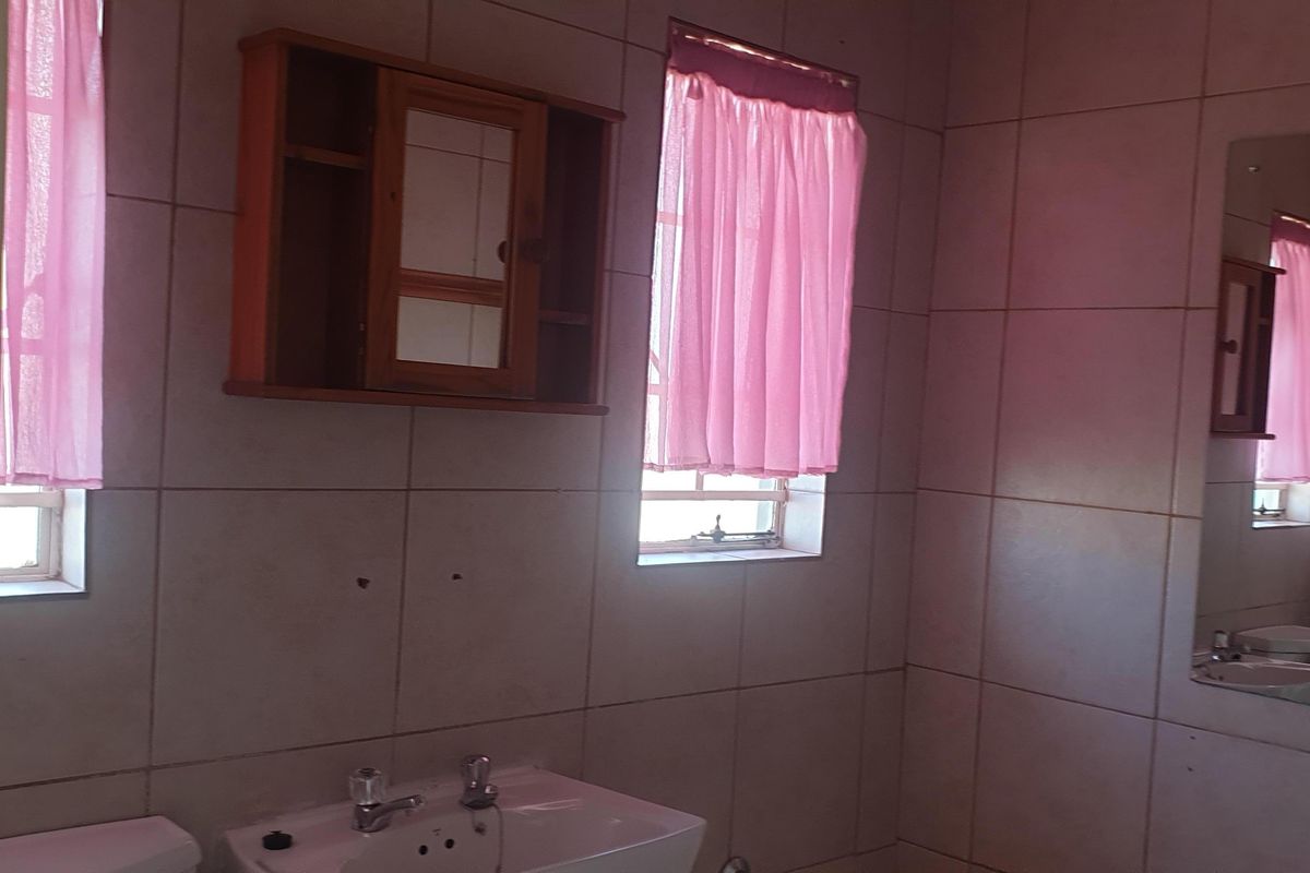 A functional bathroom featuring wall-mounted vanity mirror, basin with chrome taps, and full-height wall tiling.
