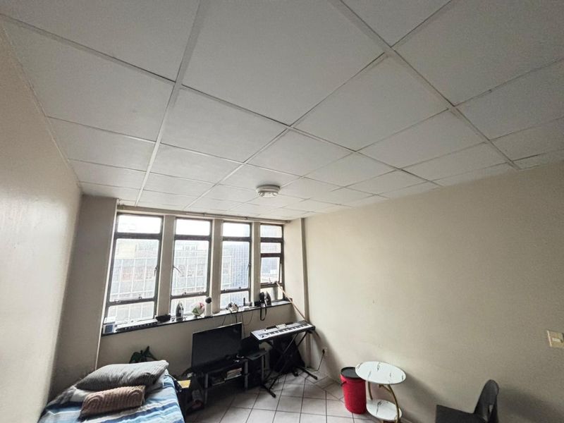A bedroom featuring a drop ceiling, tiled flooring, and large windows providing natural light and urban views.