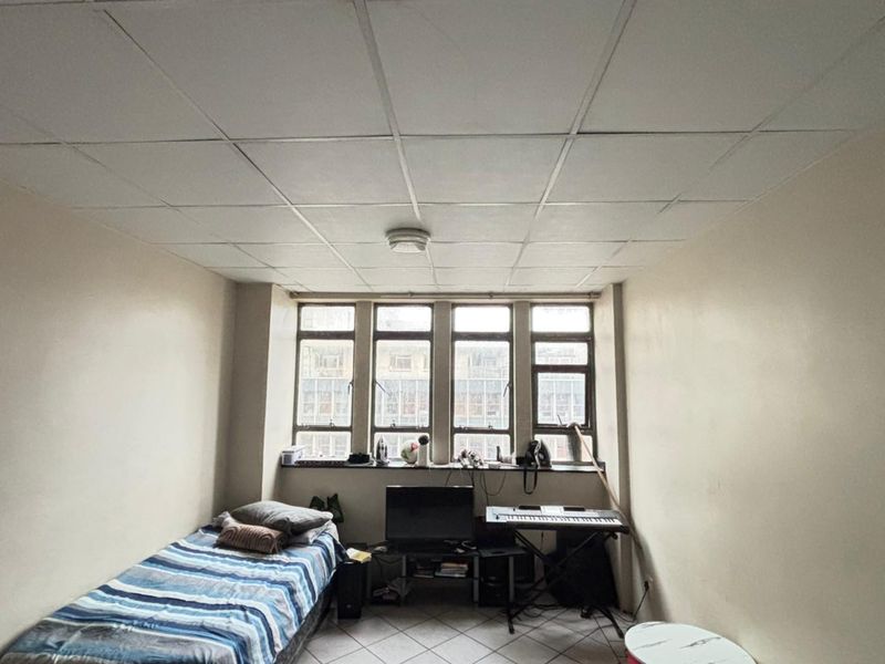 A bedroom featuring tiled flooring and a drop ceiling with a large multi-pane window providing natural light.
