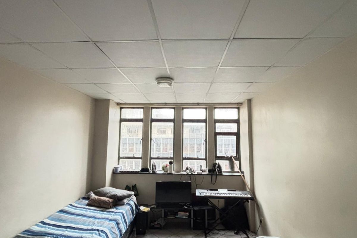 A bedroom featuring tiled flooring and a drop ceiling with a large multi-pane window providing natural light.