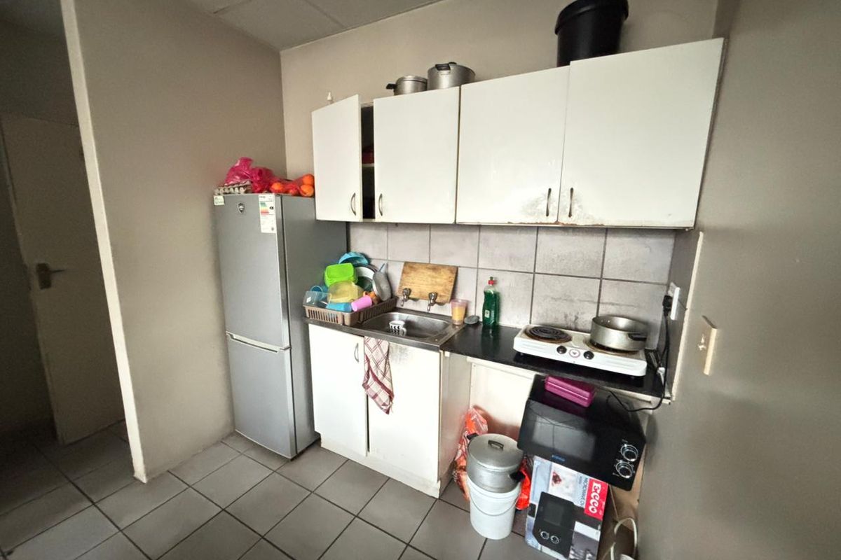 Compact kitchen area featuring built-in cabinetry, a stainless steel sink, and tiled finishes, offering a functional space in need of cosmetic updates.