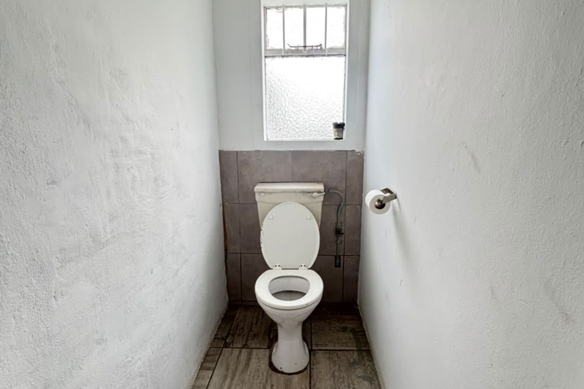 A small, dated bathroom featuring a toilet, tiled flooring, and a window. The space requires cosmetic updates to the walls and ceiling.
