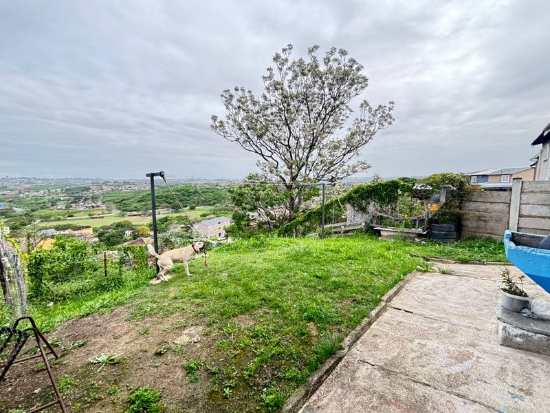 A sloped backyard area featuring a concrete patio, a precast boundary wall, and an expansive elevated view of the surrounding neighborhood.