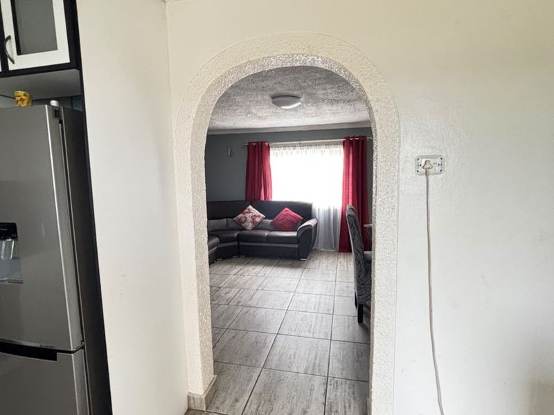 Open plan living area featuring a distinctive arched doorway, tiled flooring, and textured ceiling, connecting the kitchen space to the main living room.