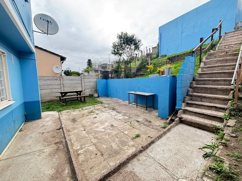 Rear outdoor area featuring a paved patio, concrete staircase, and retaining walls, offering potential for landscaping and outdoor living improvements.