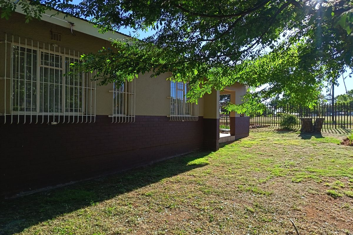 A view of the rear exterior of the house featuring a brick facade, security bars on windows, and a spacious garden area.