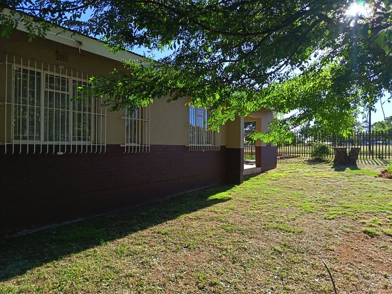 A view of the rear exterior of the house featuring a brick facade, security bars on windows, and a spacious garden area.