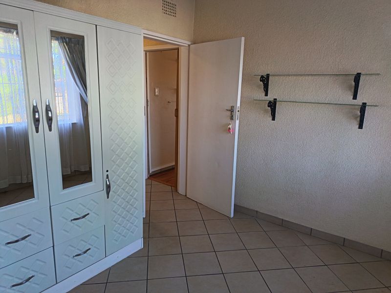 Bedroom featuring tiled flooring, a built-in wardrobe with mirrored panels, and wall-mounted glass shelving, providing functional storage and a neutral base.