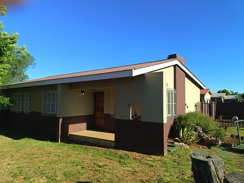 Rear view of a single-story house featuring a corrugated metal roof, brick chimney, and a small covered patio area.