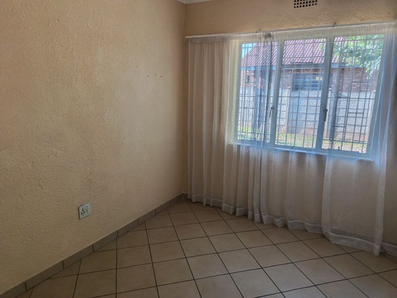 A vacant bedroom featuring neutral tiled flooring, textured walls, and a window fitted with security bars.