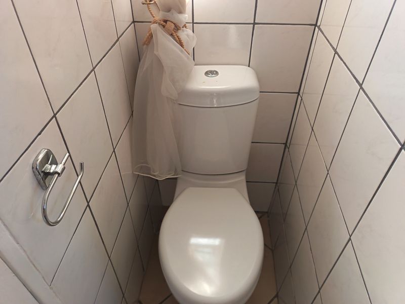 A compact, tiled bathroom featuring a standard white toilet and chrome toilet paper holder.