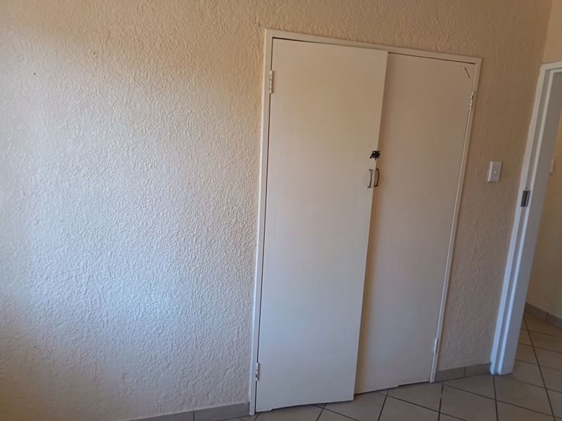 A hallway area featuring tiled flooring and a built-in cupboard with visible wear to the doors and latch mechanism.
