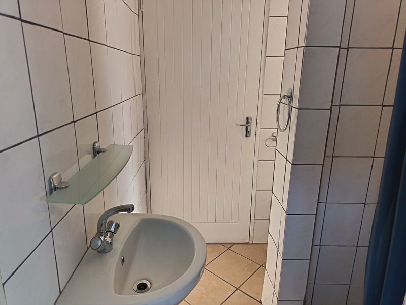 A functional bathroom featuring a wall-mounted basin, chrome fixtures, and tiled surfaces throughout.