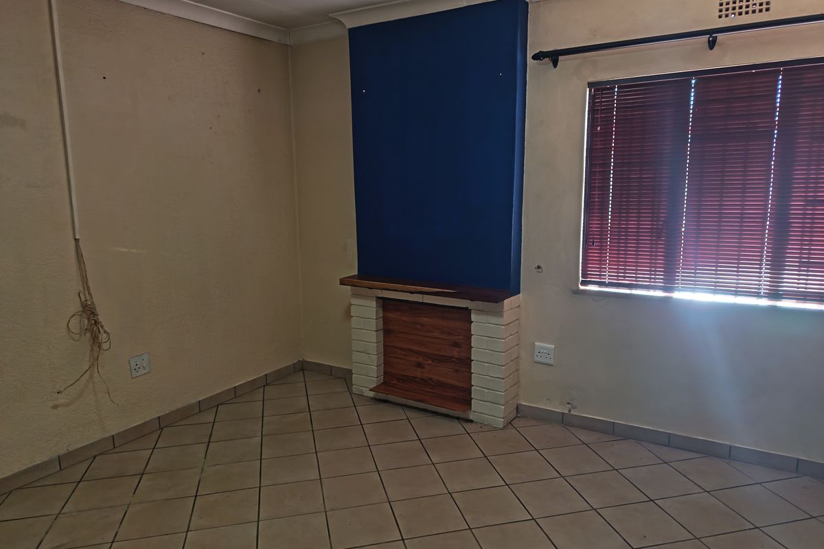 An empty living room featuring a brick fireplace, tiled flooring, and coved ceilings, requiring cosmetic updates to improve its overall appeal.