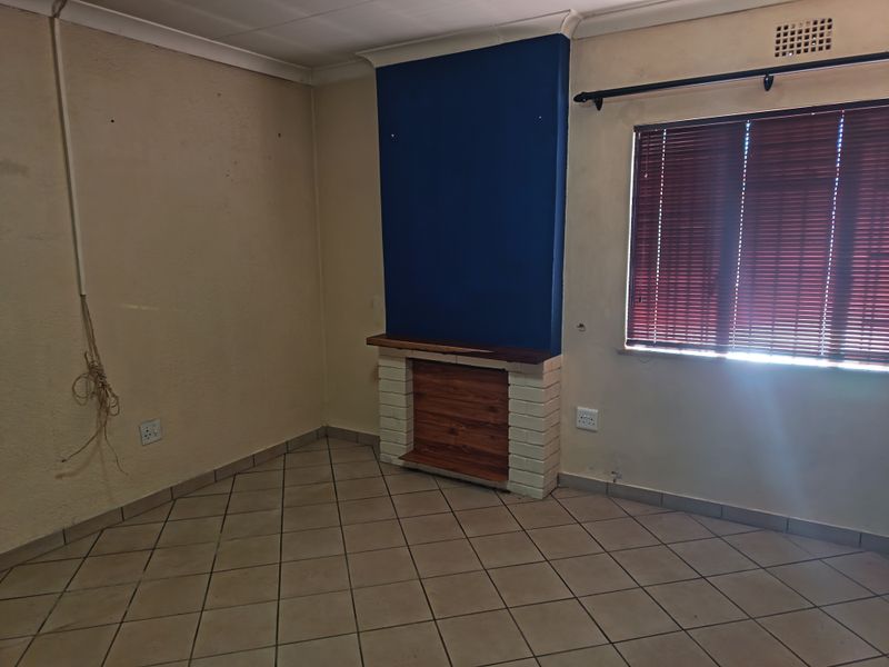 An empty living room featuring a brick fireplace, tiled flooring, and coved ceilings, requiring cosmetic updates to improve its overall appeal.