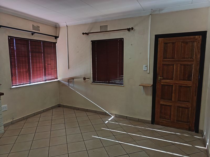 An empty living area featuring tiled flooring, timber panel door, and venetian blinds, requiring cosmetic updates to wall finishes.