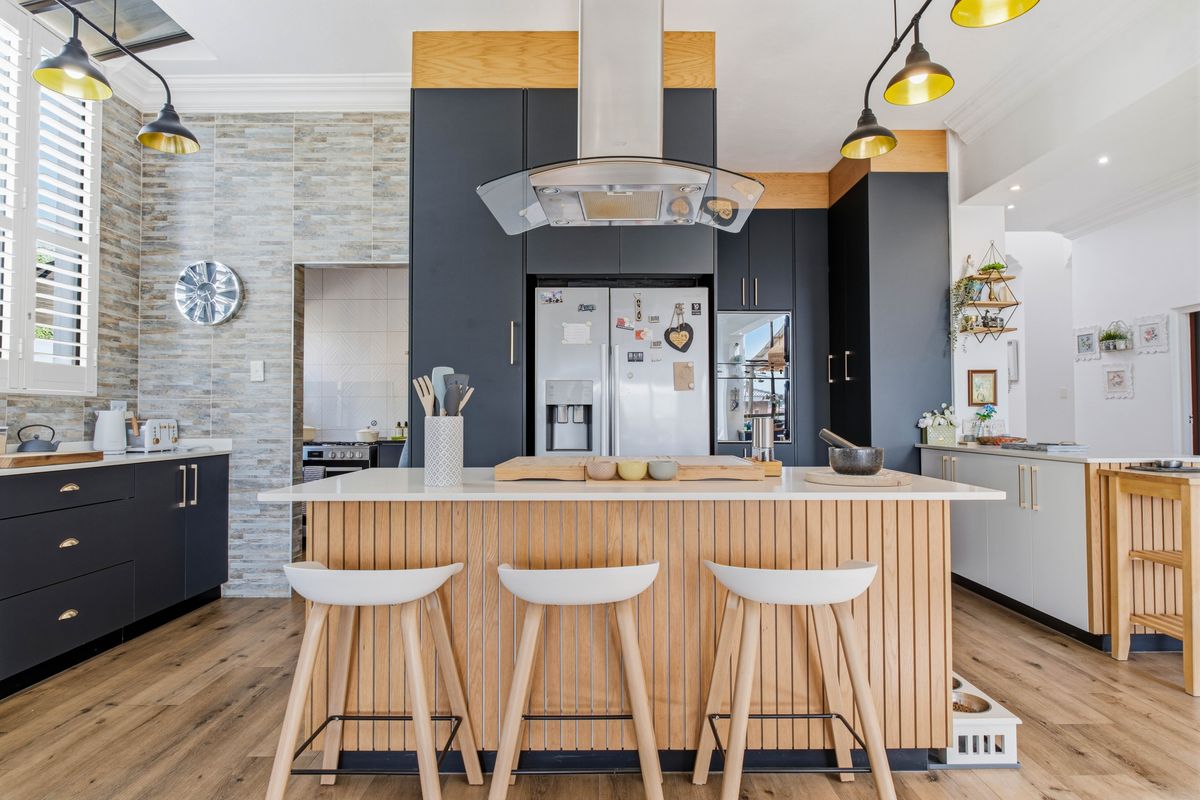 Modern kitchen featuring a central island with stone countertops, dark cabinetry, stone feature wall, and high-quality laminate flooring.