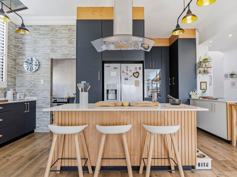 Modern kitchen featuring a central island with stone countertops, dark cabinetry, stone feature wall, and high-quality laminate flooring.