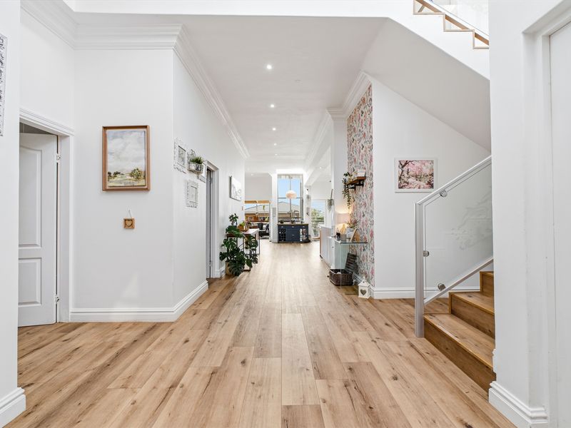 Spacious and bright entrance hallway featuring modern timber flooring, elegant crown molding, and a contemporary staircase with a glass balustrade.