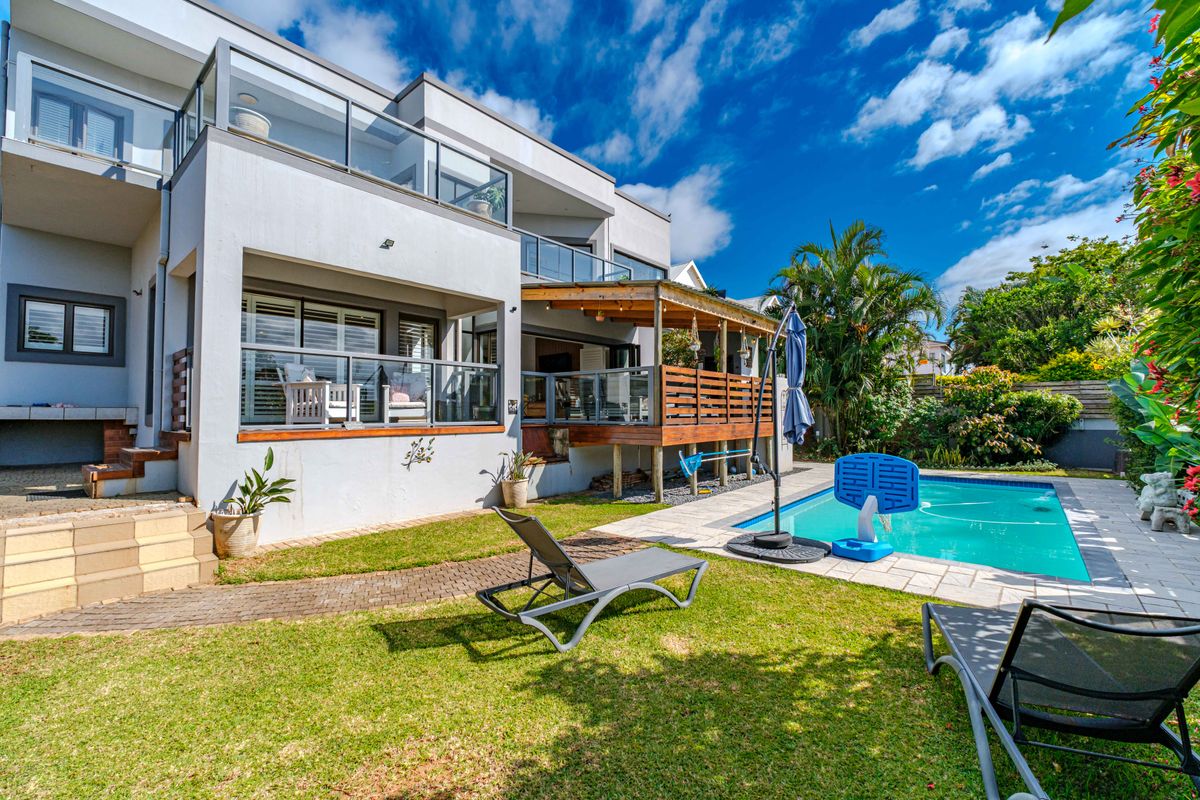 Rear view of the property featuring a swimming pool, timber deck, covered veranda, and well-maintained garden area.