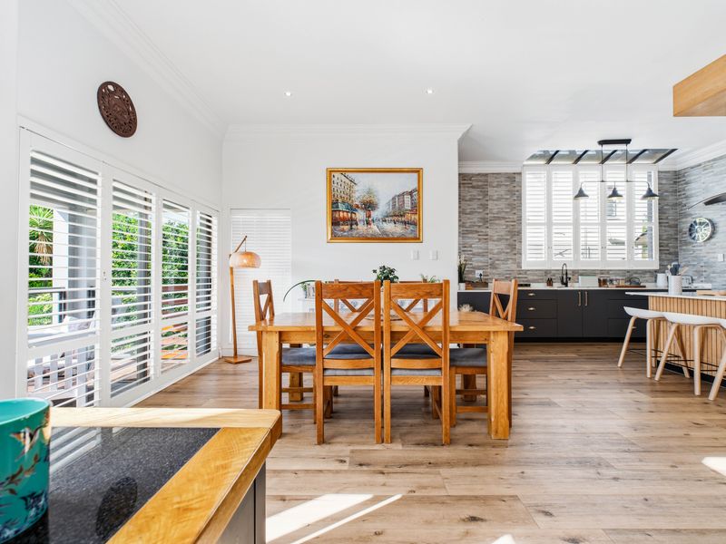 Spacious open-plan living and dining area featuring timber flooring, plantation shutters, a modern kitchen with an island, and a stylish stone feature wall.