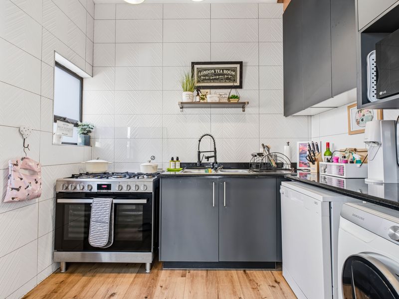 Modern kitchen featuring dark grey cabinetry, granite countertops, a gas stove with oven, and stylish herringbone-patterned wall tiling.